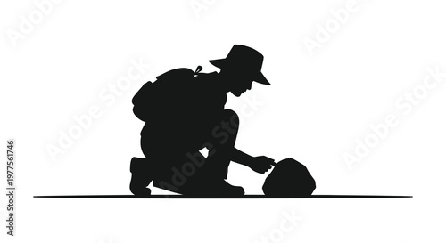 Hiker examining a rock kneeling with backpack stark black silhouette