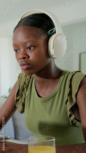 Vertical video: Phone pinging, teen typing at home table in green top with laptop, headset, juice