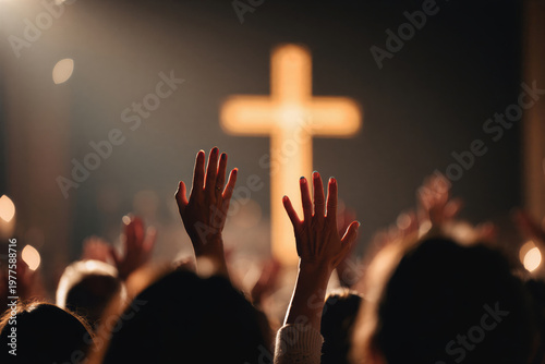 People raise their hands in worship in front of a large illuminated cross in a church