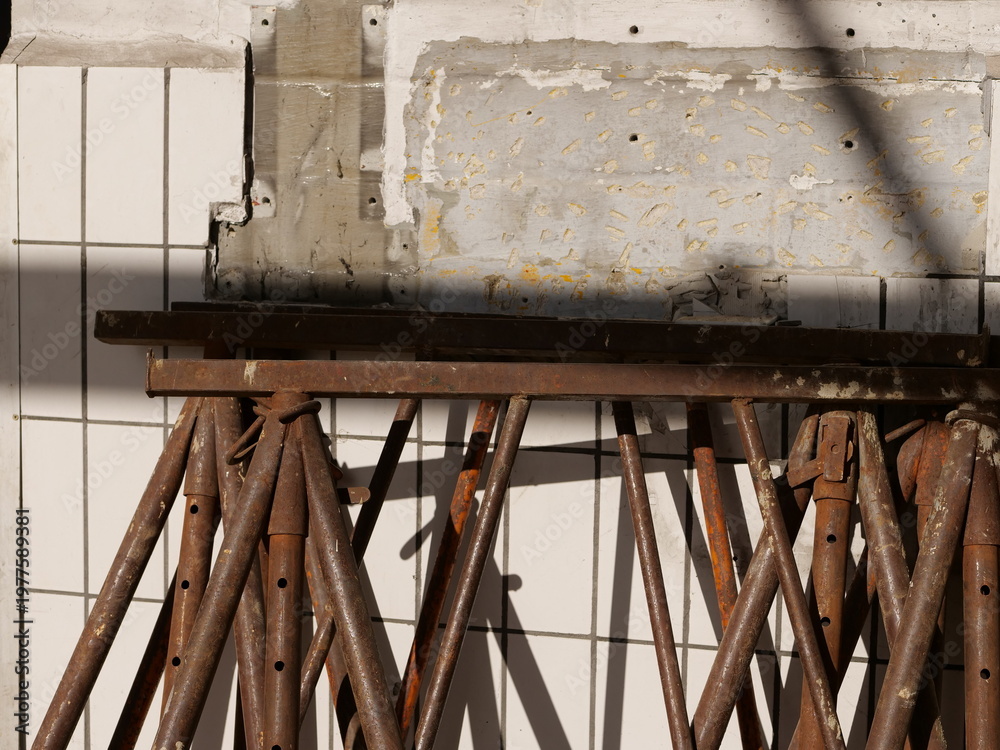 Obraz premium several rusted steel construction props leaning against a wall during a renovation. The background features a section of white square tiles and a rough grey concrete patch where tiling has been remove