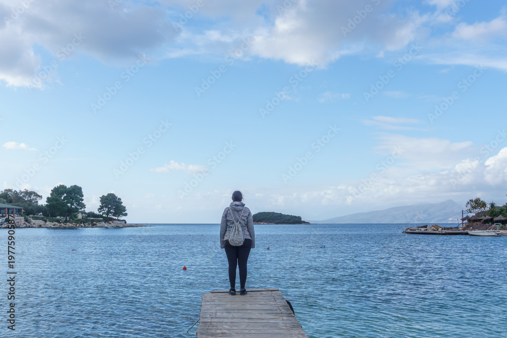 Fototapeta premium One person standing at the end of a wooden pier in the water on a beach at Adriatic sea coast in Ksamil, Saranda, Albania