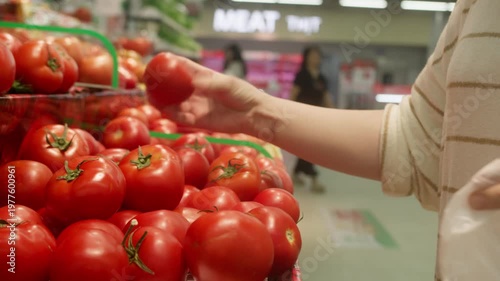 Woman choosing red tomatoes in supermarket produce section.