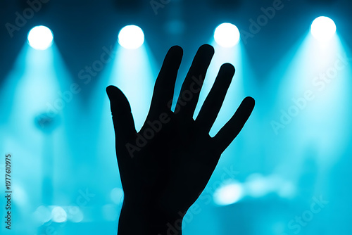 Silhouetted Hand Raised Under Vibrant Blue Stage Lights at Live Event