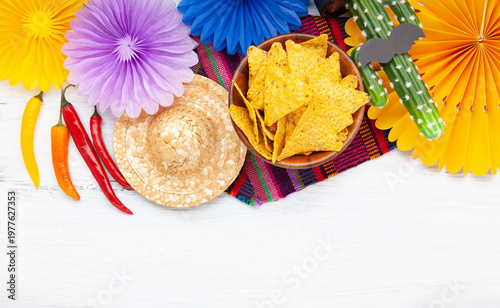 Cinco de Mayo festive composition with tortilla chips, chili peppers, cactus with sombrero and mustache and traditional Mexican textile on white wooden background