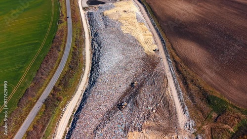 Wide aerial view of large scale municipal solid waste landfill. Drone perspective showing the extent of garbage disposal site adjacent to agricultural land.