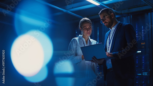 IT professionals working on laptop in server room, managing data center network and cloud infrastructure