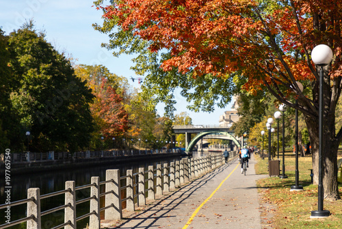 Recreational trail along water during autumn season. People cycling and walking on park path near Rideau Canal in fall