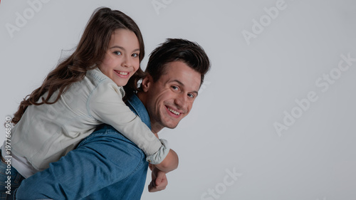 Smiling father giving his happy daughter a piggyback ride while looking at camera isolated on white background. Family bonding, love, fun, care and playful parenting concept.