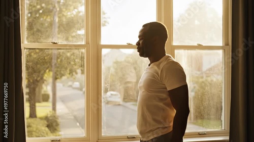 Man stretching and talking on phone by window at sunrise.