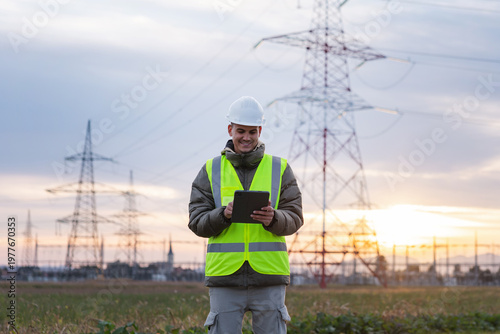 Tableau sur toile Young male electrical engineer uses a tablet to inspect high voltage lines in an outdoor area during the evening