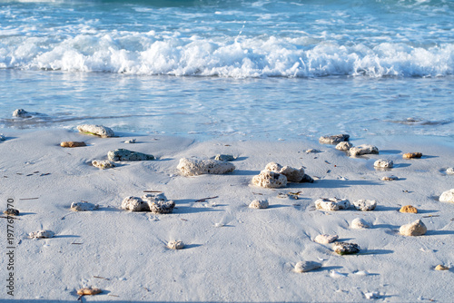 Seascape. Snow-white sand. Small stones and pebbles of various shapes and sizes are scattered across the sand, some of which are coated with sea salt, giving them a slightly rough texture. Gentle wave