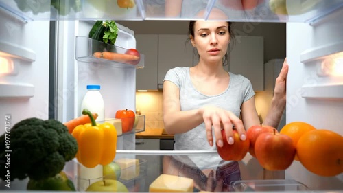 Woman looking for food in a refrigerator at night.