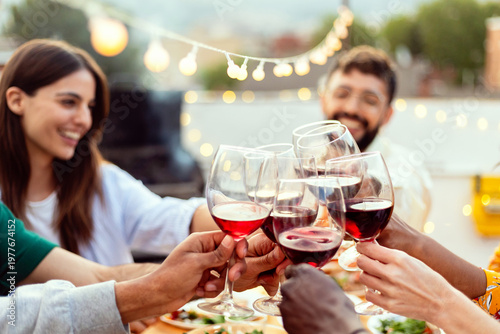 Foto Group of diverse friends celebrating and toasting with red wine glasses during a