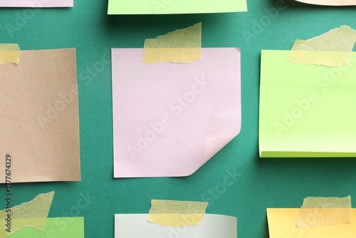 Blank paper notes with adhesive tape on green background, top view