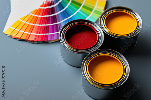 Top view of three open paint cans in orange red, purple with a paintbrush and rainbow color swatch fan on dark background