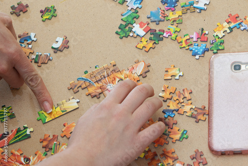 A teenage girl and her mother are putting together a puzzle in natural light. Only their hands are visible.