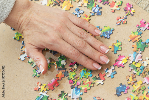 A woman is assembling puzzles at home in natural light. Only hands are visible.