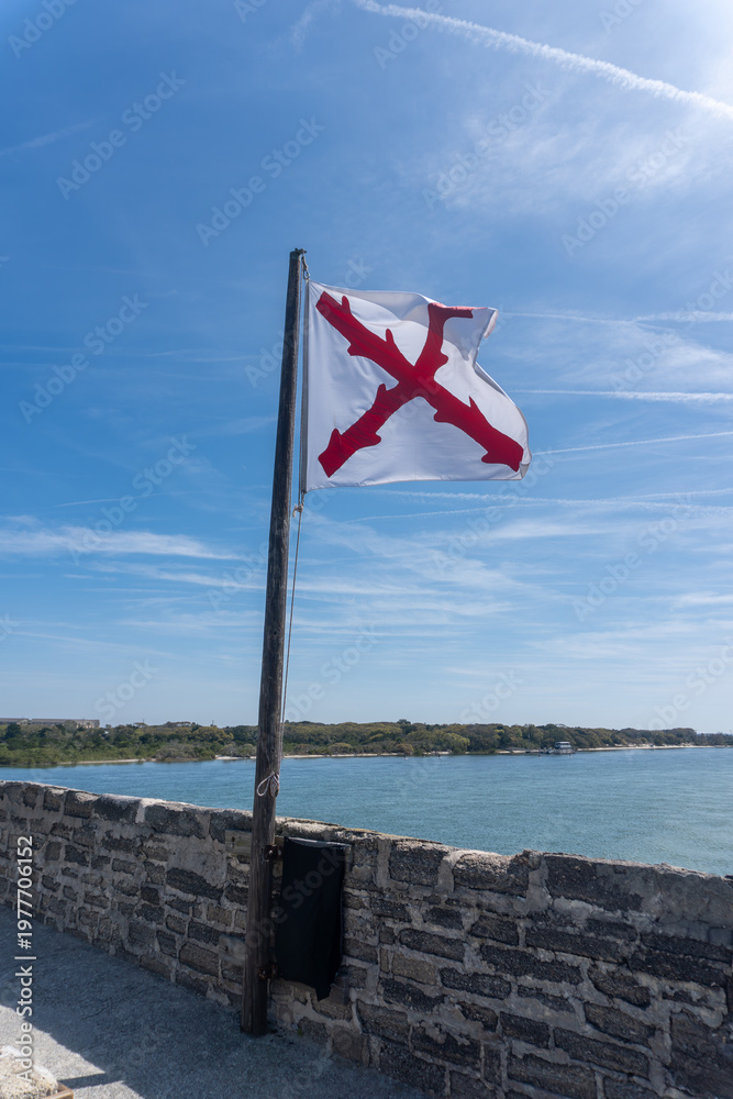 Fototapeta premium Cross of Burgundy, Spanish colonial military flag flying over Fort Matanzas National Monument in St. Augustine, Florida. Spanish fort to guard Matanzas Inlet in conjunction with Castillo de San Marcos