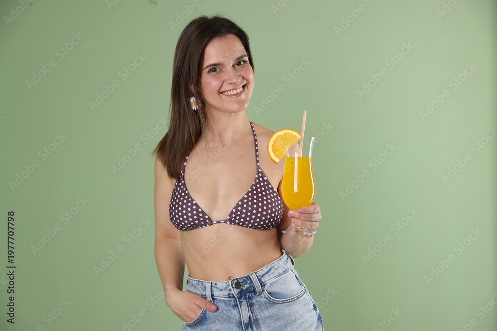 Fototapeta premium Beautiful woman with cocktail wearing stylish swimsuit on green background
