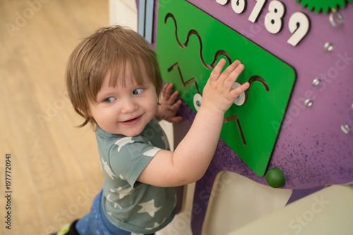 Photos Toddler boy aged 15 months playing with a sensory busy board on the wall in a kids play area