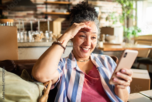 Smiling mature woman video chatting on smartphone at home