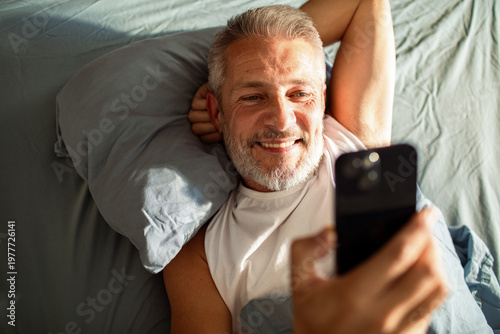 Smiling mature man video calling in bed at home