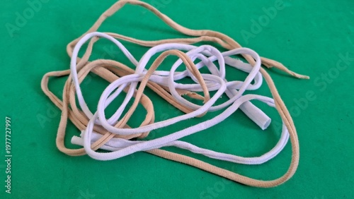 A jumbled heap of soft white and beige fabric cords tangled together on a plain green surface.