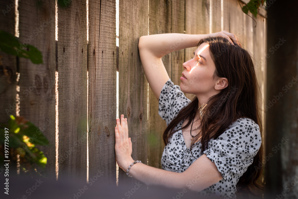 Obraz premium Young woman by wooden fence in warm sunlight