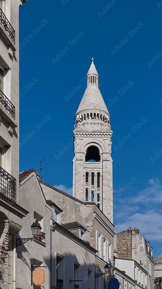 Fototapeta premium Sacre Coeur basilica tower rising above Montmartre roofs under blue spring sky