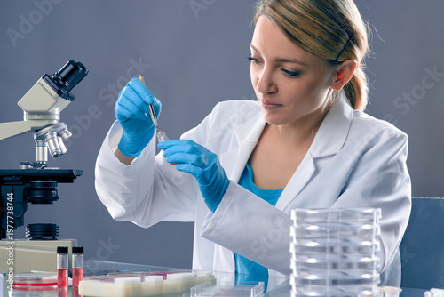 Young european female scientist pipetting with micropipette beside compound microscope in lab