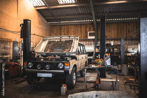 Foto Classic 4x4 undergoing repairs in a cluttered workshop with car lift