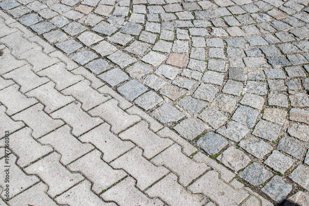 Fototapeta premium Diagonal transition between cobblestone and concrete pavement creating contrasting urban texture background with geometric structure