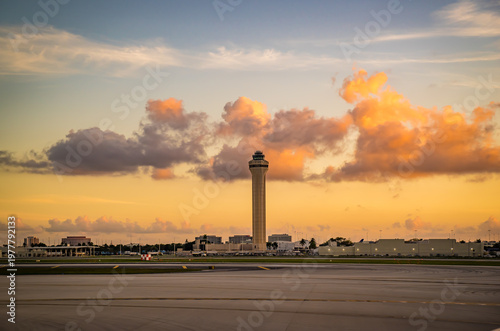 Beautiful sunset at Miami International Airport. The airport traffic air control tower is bathed in orange sunlight. The tower is surrounded by a magnificent cover of clouds
