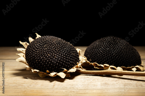 Dried sunflower heads with black seeds on wooden table.