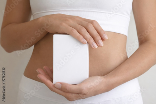 Young woman's torso, hands holding a small white box, plain white bra