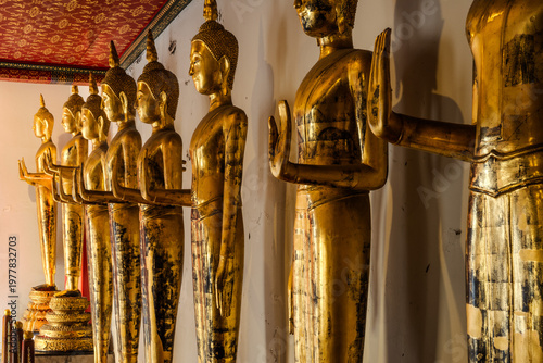 Golden Buddha statues standing in a row along a temple corridor at Wat Pho, Bangkok. Traditional Thai architecture with ornate details, warm lighting, and a serene spiritual atmosphere.