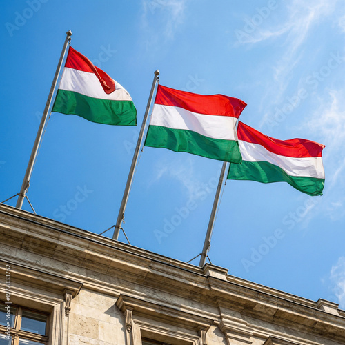 three national flags of hungary waving on poles on top of an old historic building against a clear blue sky as a symbol of statehood and national holidays