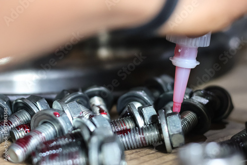 Photos Technician applying red threadlocker adhesive to heavy duty bolt threads during industrial workshop assembly