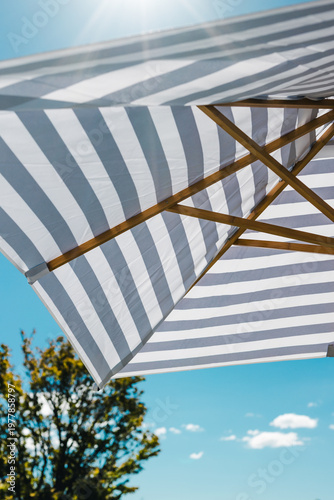 striped blue and white sun umbrella with sunflare with serene sky in the background