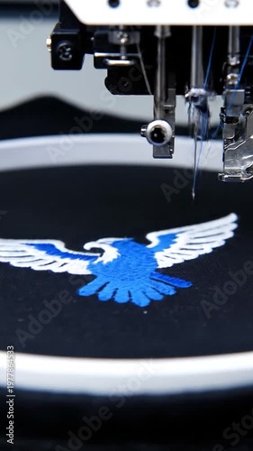 A professional industrial machine creates a detailed blue bird embroidery design on black fabric