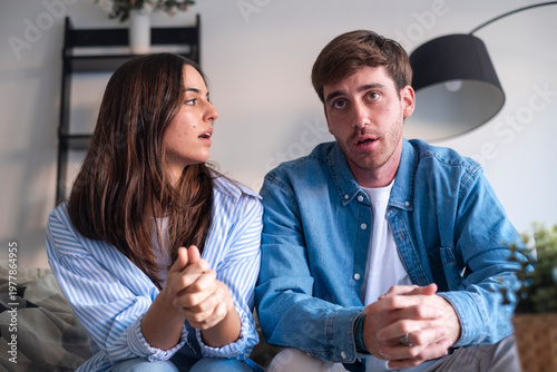 Bild auf Leinwand Young couple sitting together on a sofa at home, engaged in a tense conversation