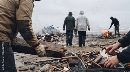 Group activity collecting driftwood and tending a campfire on a rugged beach under an overcast sky.
