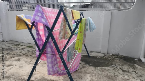 Colorful Laundry Drying On A Rack Outdoors In Bright Sunlight With A Grated Metal Fence Overhead