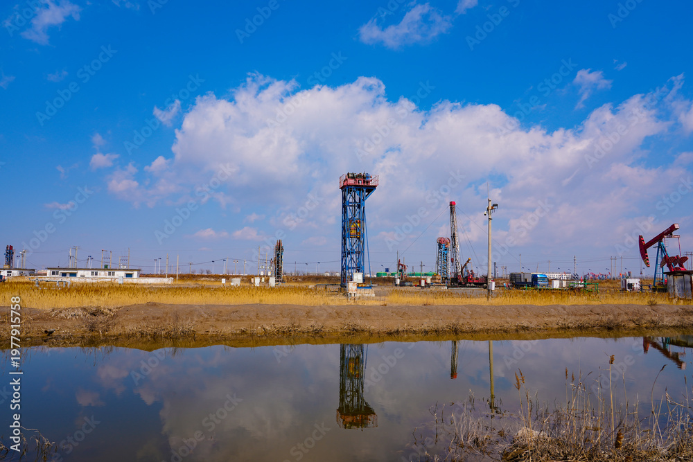 Obraz premium Oil pump in operation with blue sky and white clouds