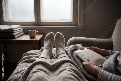 Woman's feet in socks with hot water bottle relaxing at home