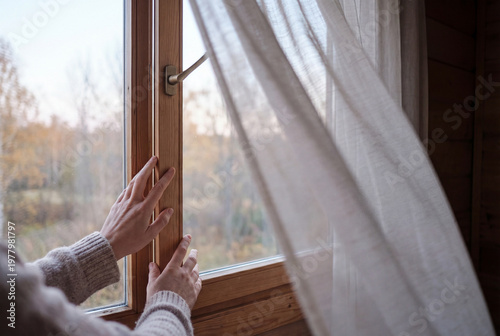 Woman's hands gently touching a rustic wooden window frame at home