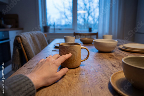 Hand touching a ceramic mug on a wooden table in a home