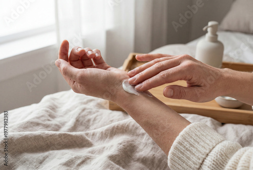 Woman applying hand cream for skin care in bed