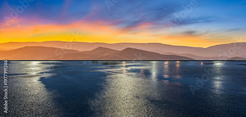 Wet asphalt road reflecting vibrant sunset colors over rolling hills landscape