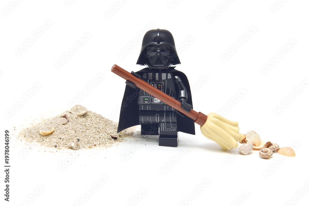 Fototapeta premium Lego minifigure of peaceful Darth Vader from Star Wars is cleaning a sand from seashell isolated on white. Editorial illustrative image of stop war concept.